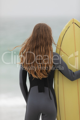 Female surfer standing with surfboard on the beach