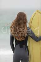 Female surfer standing with surfboard on the beach