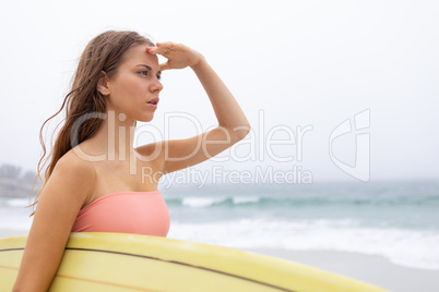 Female surfer standing with her surfboard on the beach