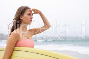 Female surfer standing with her surfboard on the beach