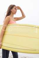 Female surfer standing with her surfboard on the beach