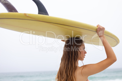 Female surfer carrying surfboard on her head at beach