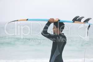 Male surfer carrying surfboard on her head at beach