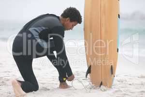 Male surfer tying surfboard leash on his leg at beach