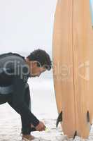 Male surfer tying surfboard leash on his leg at beach