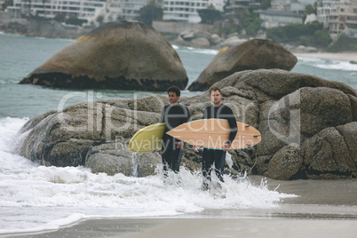 Male friends standing on beach while holding surfboard