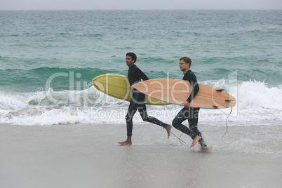 Male friends running on beach while holding surfboard