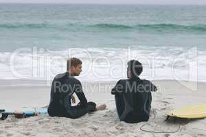 Male friends sitting on beach while interacting with each other