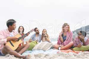 Man playing guitar while friends enjoying on beach