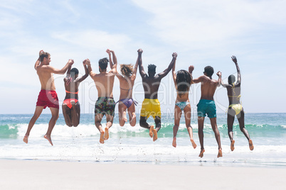 Group of friends enjoying and jumping in water at beach on a sunny day