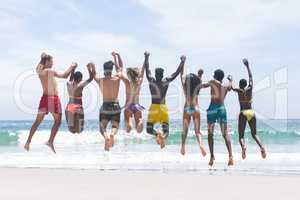 Group of friends enjoying and jumping in water at beach on a sunny day