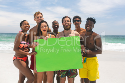 Multi-ethnic group of friends holding a empty green placard at beach on a sunny day