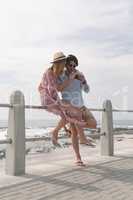 Caucasian couple reviving photos while sitting at railing on beach
