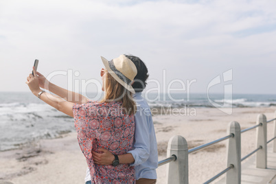 Caucasian couple taking selfie while standing near sea side at promenade