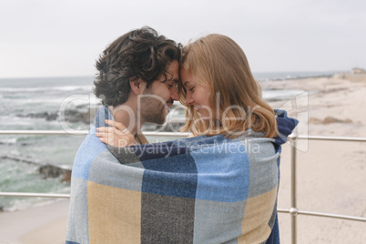 Caucasian couple wrapped in blanket standing at promenade near beach