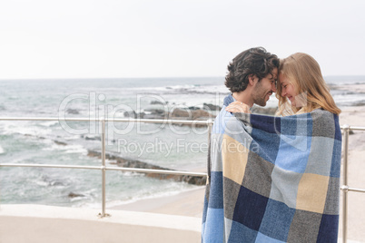 Caucasian couple wrapped in blanket standing at promenade near beach