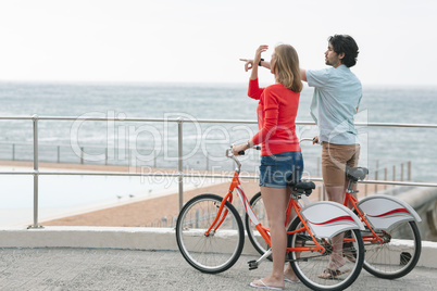 Caucasian couple interacting with each other while holding bicycle at promenade