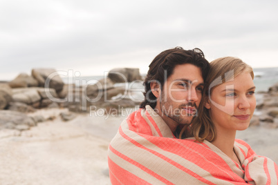 Caucasin couple wrapped in blanket standing at  beach