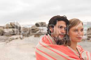 Caucasin couple wrapped in blanket standing at  beach