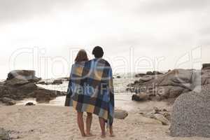 Caucasian couple wrapped in blanket standing at beach