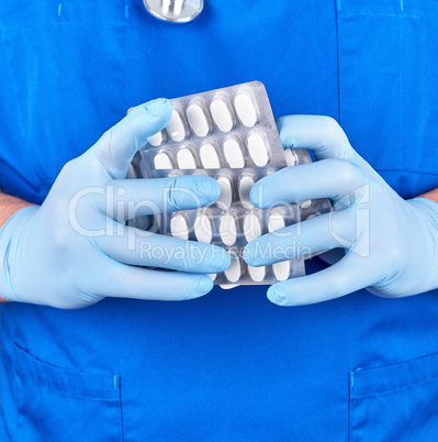 doctor in blue uniform and sterile gloves holding white pills in