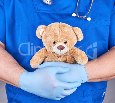 doctor in blue uniform and  latex gloves holding a brown teddy b