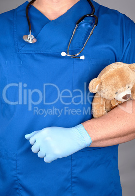 doctor in blue uniform and  latex gloves holding a brown teddy b