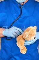 doctor in blue uniform and latex gloves holding a brown teddy be