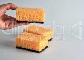 hand is holding a yellow kitchen sponge for washing dishes