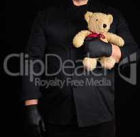 man in a black uniform holds in his hand a toy teddy bear