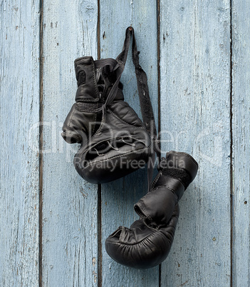 pair of very old leather black boxing gloves hanging on a nail