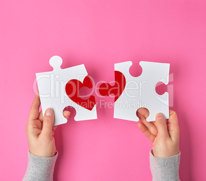 Female hands hold big white puzzles with a piece of red heart