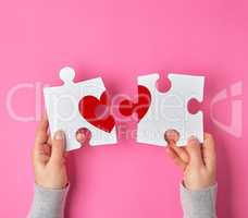Female hands hold big white puzzles with a piece of red heart