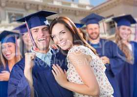 Proud Male Graduate In Cap and Gown with Girl Among Other Graduates