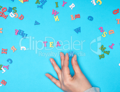 female hand and multicolored wooden letters of the English alpha