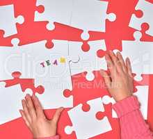 female hand puts white big puzzles on a red background