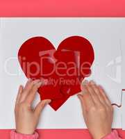 Female hands hold big white puzzles with a piece of red heart