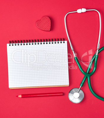 open blank notepad and green medical stethoscope on red backgrou