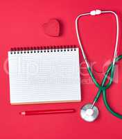 open blank notepad and green medical stethoscope on red backgrou