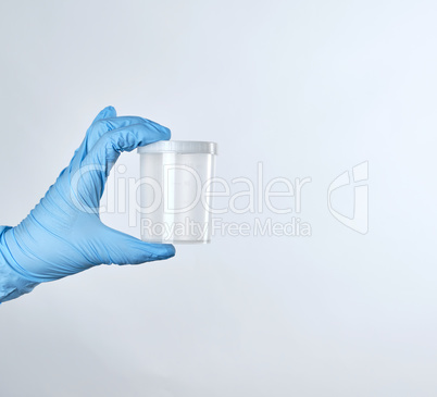 hand in a blue sterile glove holds a empty plastic container for