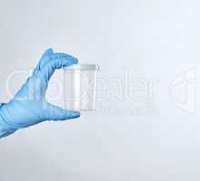 hand in a blue sterile glove holds a empty plastic container for