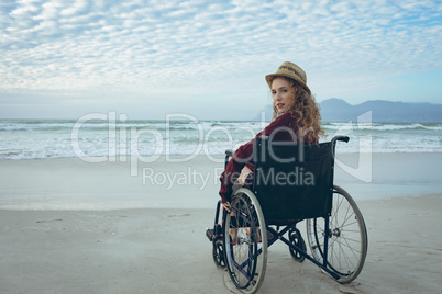 Disabled woman looking at camera sitting on wheelchair at beach