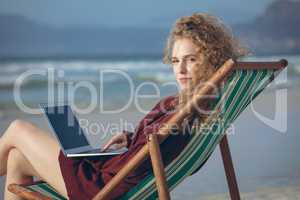 Woman using laptop while sitting on sun lounger at beach