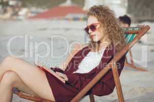 Woman reading book while sitting on sun lounger at beach
