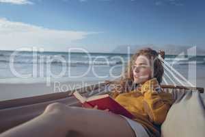Woman holding book while lying on hammock at beach