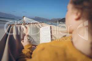 Woman reading book while lying on hammock at beach