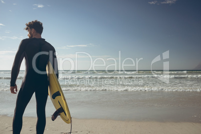 Male surfer with a surfboard standing on a beach