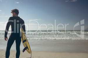 Male surfer with a surfboard standing on a beach