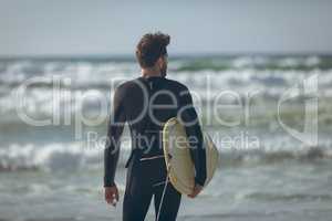 Male surfer with a surfboard standing on a beach