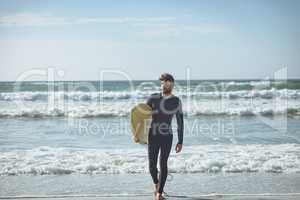 Male surfer with a surfboard walking on a beach